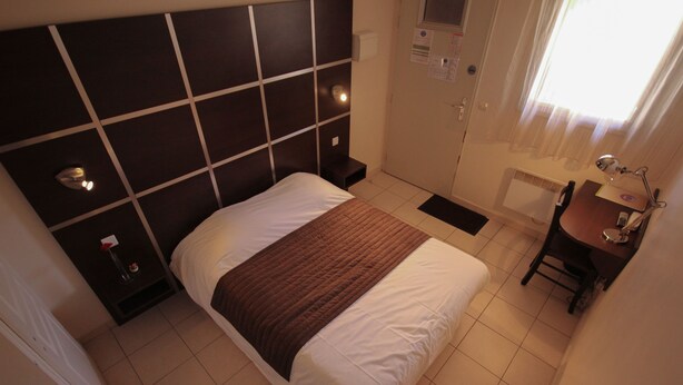 Une chambre d’hôtel avec un grand lit, une table de chevet, un bureau avec une chaise et une fenêtre avec des rideaux.