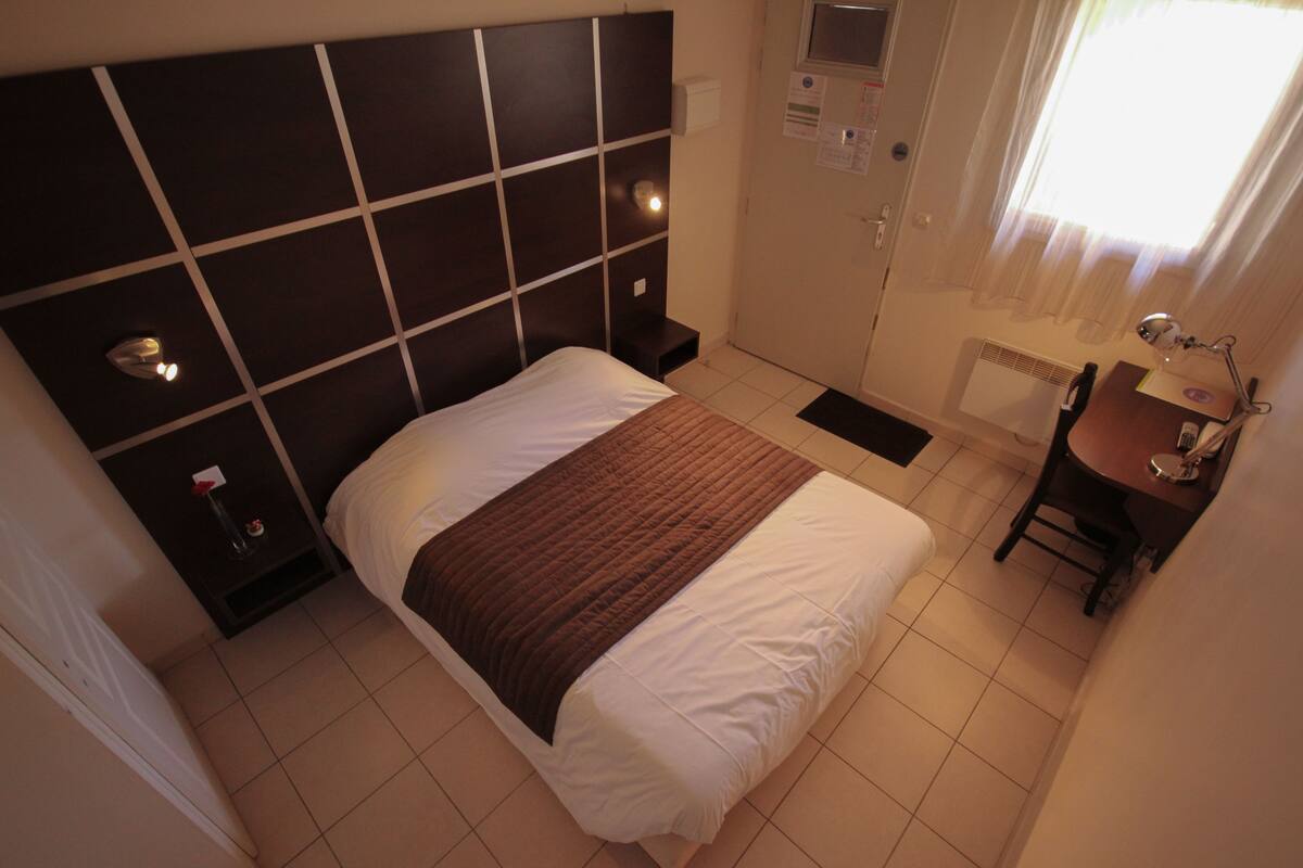 Une chambre d’hôtel avec un grand lit, une table de chevet, un bureau avec une chaise et une fenêtre avec des rideaux.