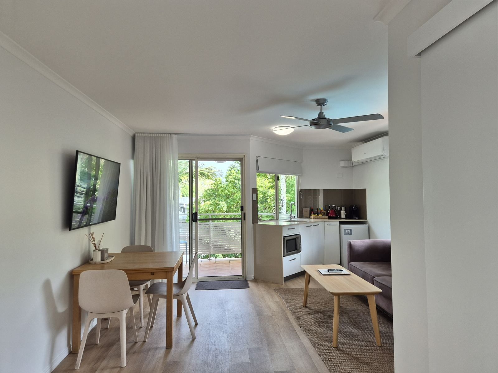 Une cuisine moderne dotée d’un four encastré, un coin repas avec une table et des chaises en bois, un canapé et un ventilateur de plafond.