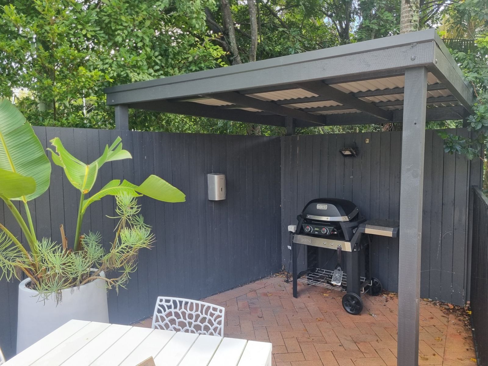 A patio with a grill, a white table, and potted plants.
