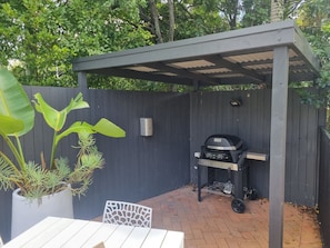 A patio with a grill, a white table, and potted plants.