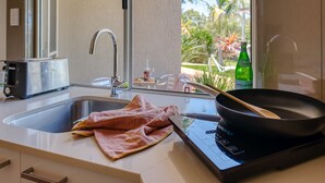A modern kitchen with a built-in stove, a sink, and a window with a view of palm trees.