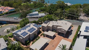 A modern building with solar panels, surrounded by lush greenery and a view of a lake with boats.