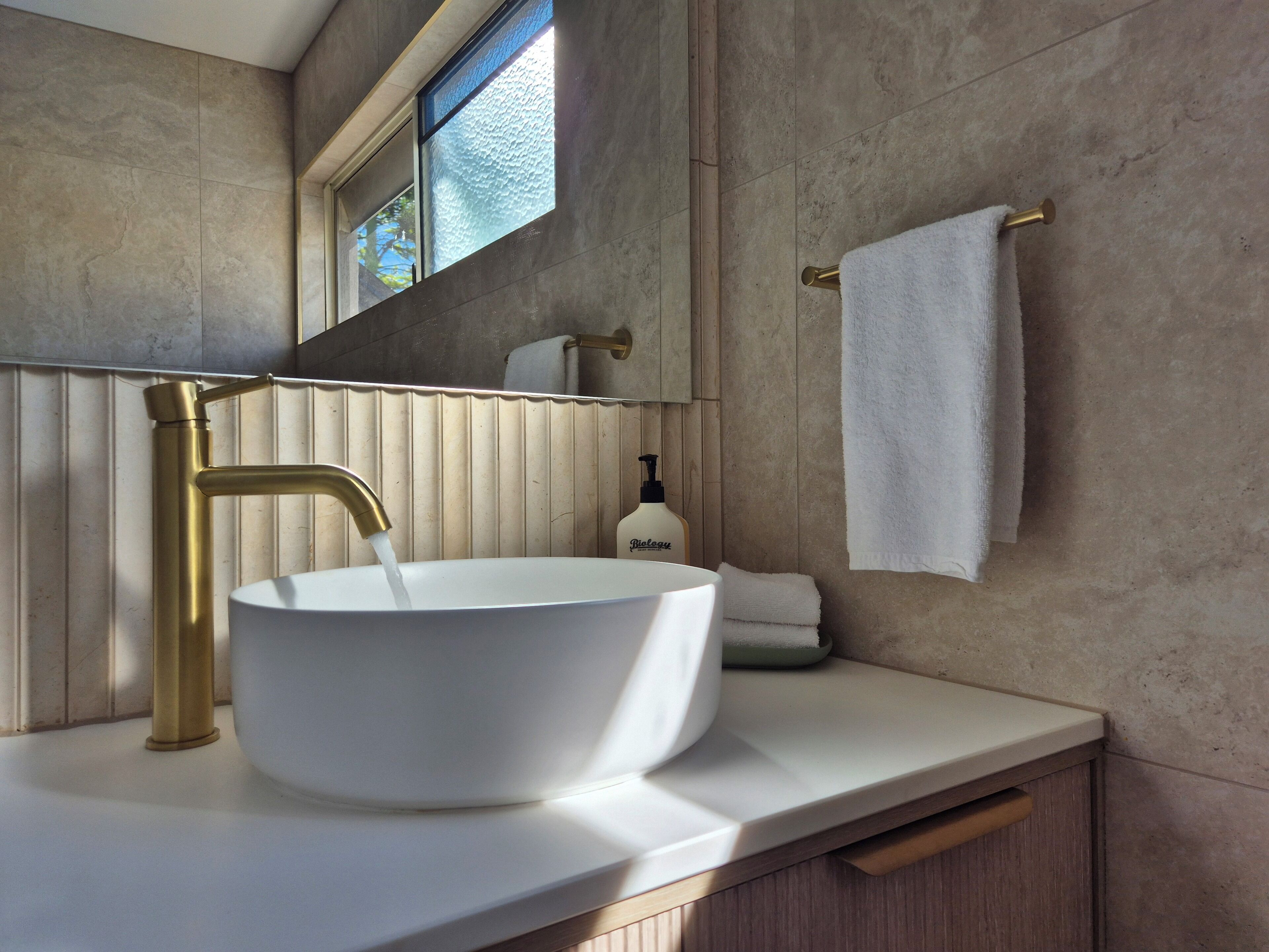 Un baño moderno con un lavamanos blanco, grifo dorado y un perchero para toallas.