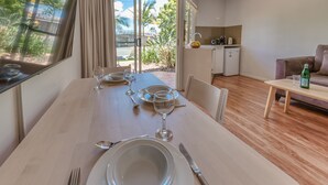 A dining area with a table set for four, a kitchen in the background, and a view of a garden through the sliding glass door.