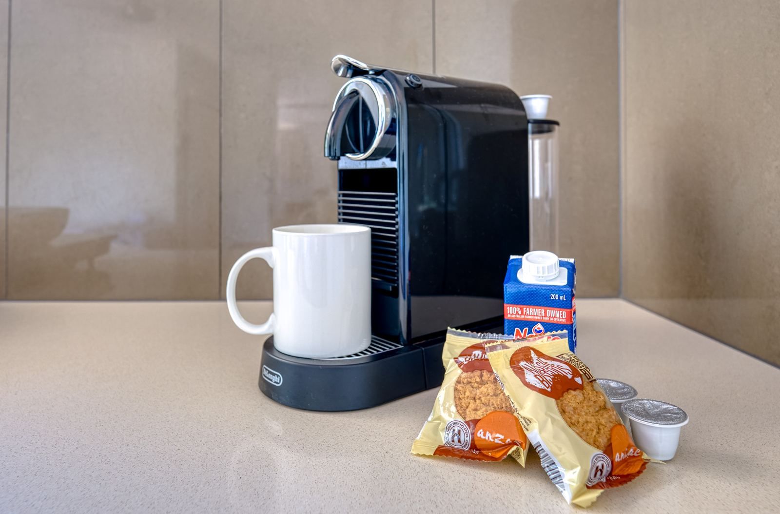 A coffee maker, a white mug, a carton of milk, and packets of snacks on a countertop.