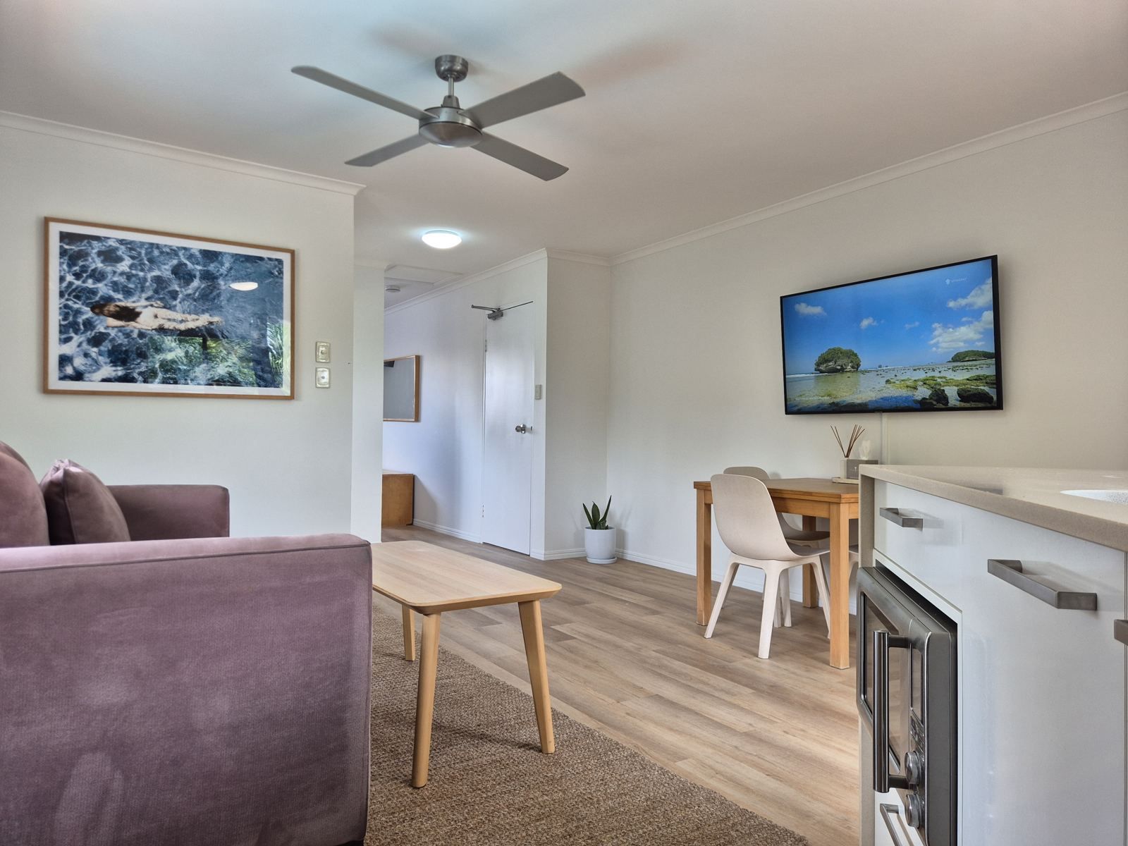 Un salon moderne comprenant un canapé, une table à manger avec des chaises, un coin cuisine avec une cuisinière et un ventilateur de plafond.