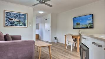 Un salon moderne comprenant un canapé, une table à manger avec des chaises, un coin cuisine avec une cuisinière et un ventilateur de plafond.