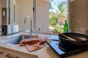 Una cocina moderna con un lavamanos de acero inoxidable, un tostador y una sartén sobre una cocina de inducción.