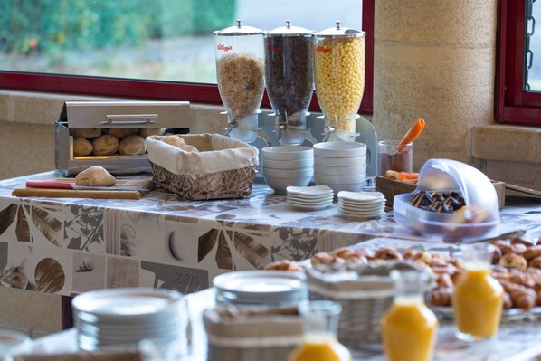 A buffet setup with various food dispensers, plates, and a basket of bread.