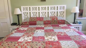 A bed with a patchwork quilt, a white headboard, two bedside tables with lamps, and a framed picture on the wall.