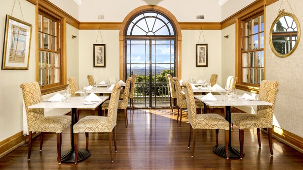 Un comedor con un amplio ventanal de arco, paneles de madera y sillas estampadas.