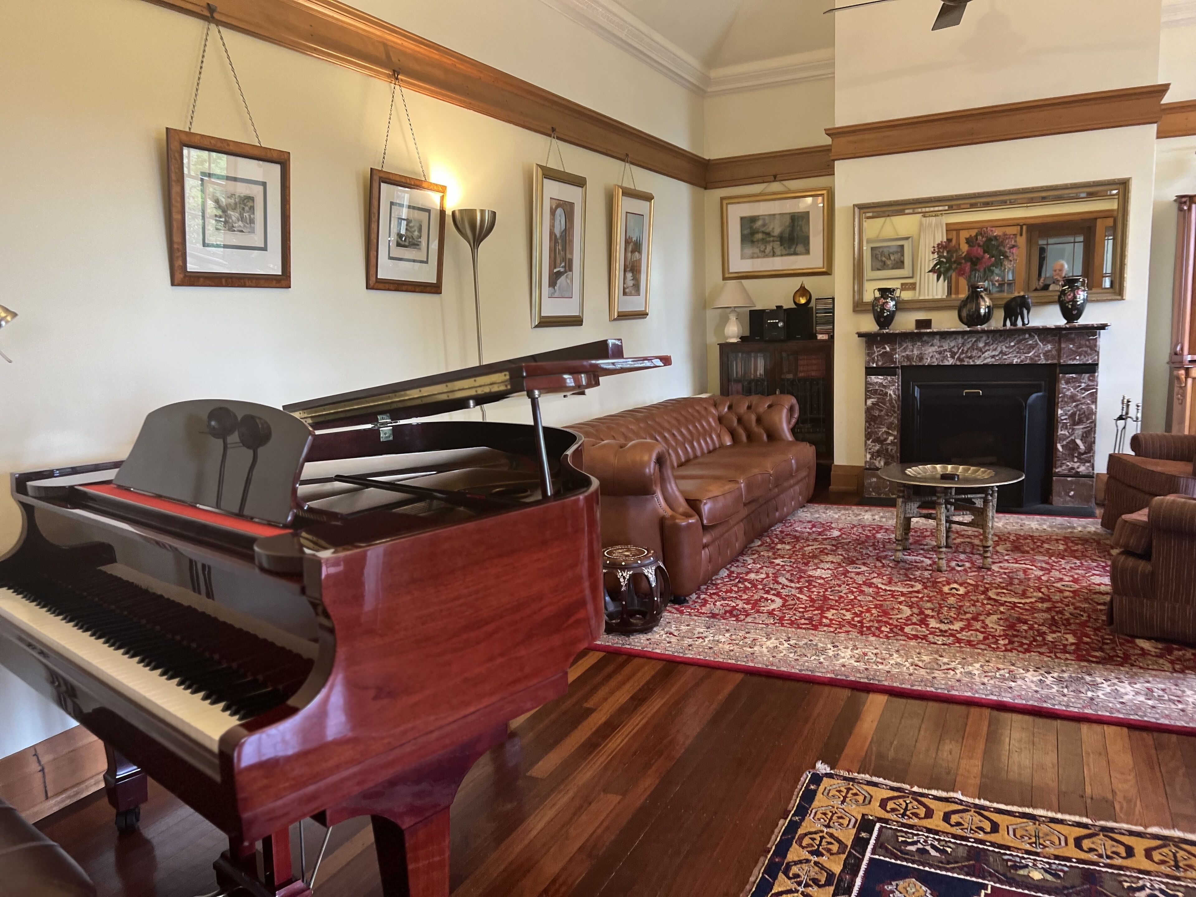 Un piano de cola, un sofá de cuero marrón, un tapete estampado y una chimenea en una sala de estar elegantemente decorada.
