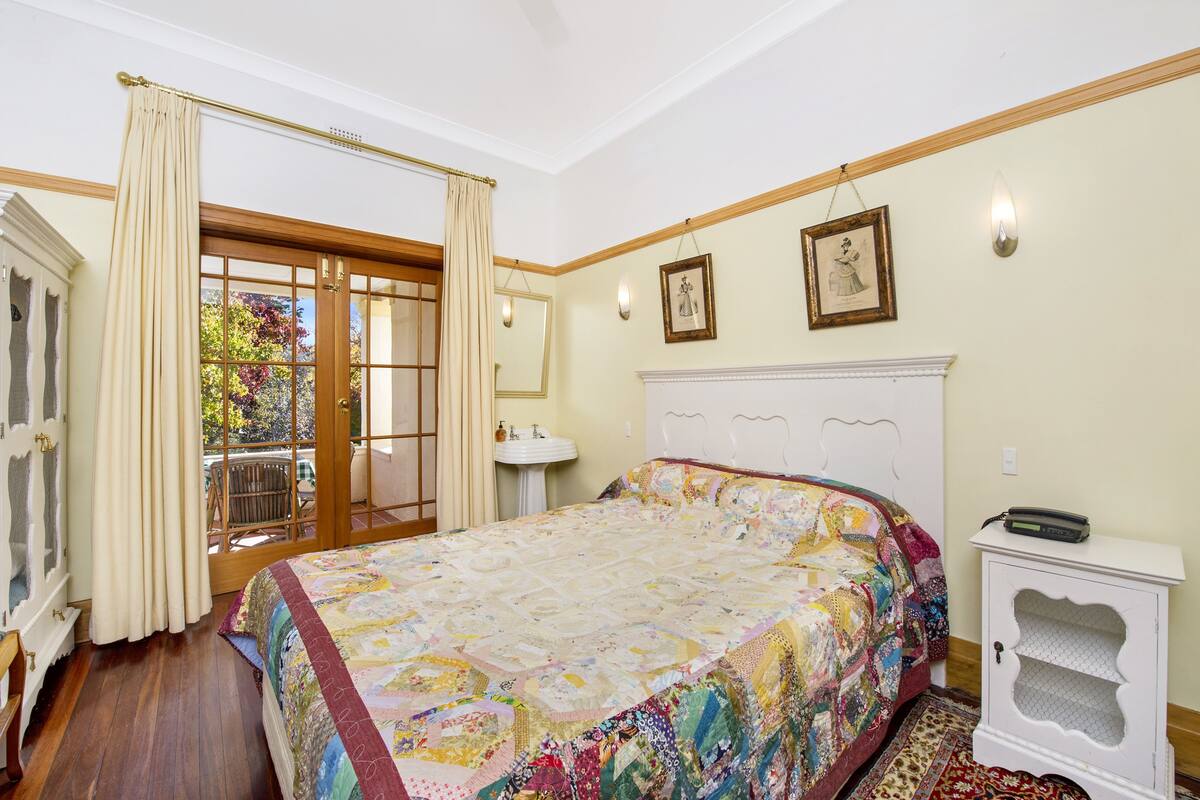 A bedroom with a large bed, a bedside table, a window with curtains, and a view of the outdoors.