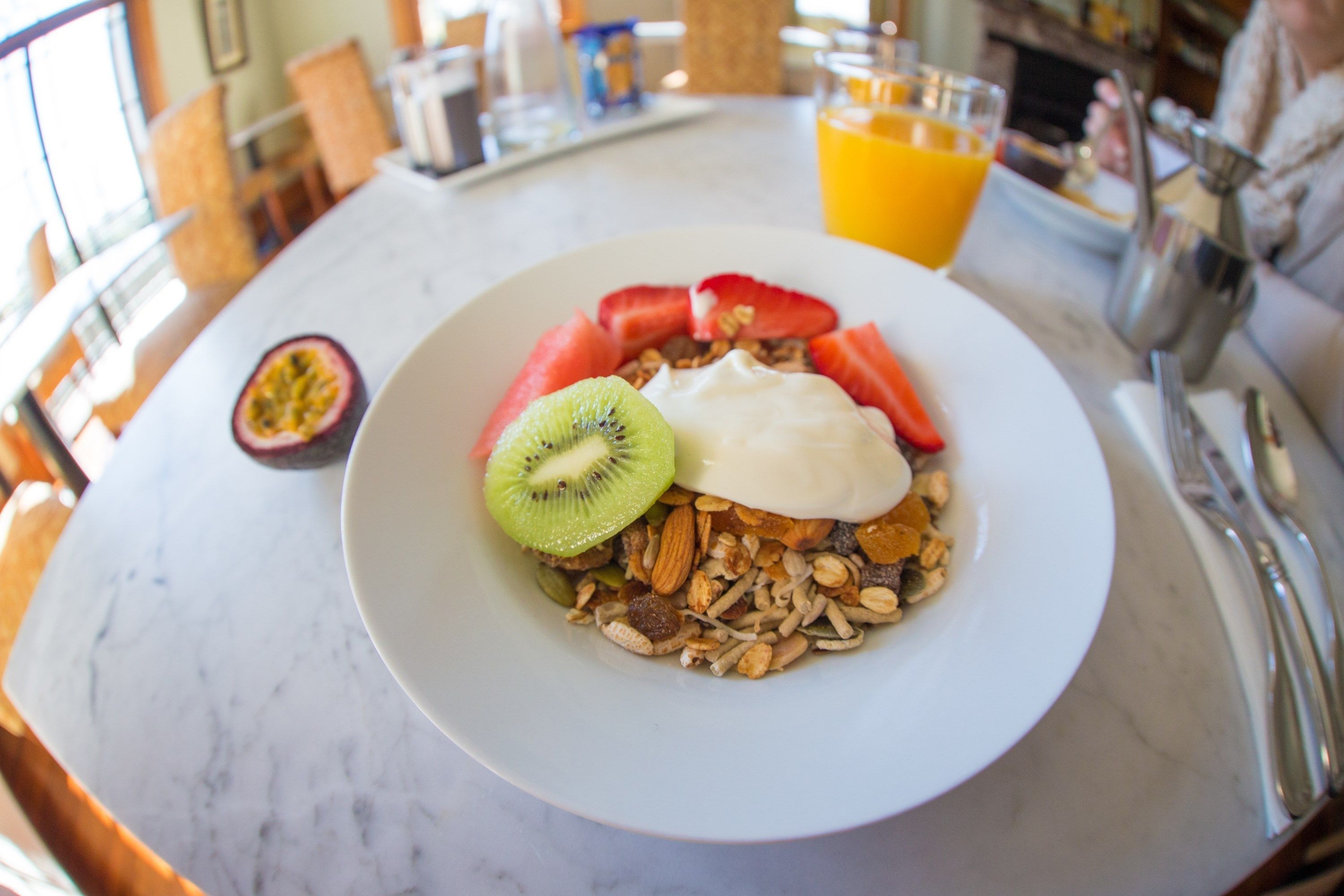 Un plato de desayuno con yogur, kiwi, fresas y granola sobre una mesa de mármol.