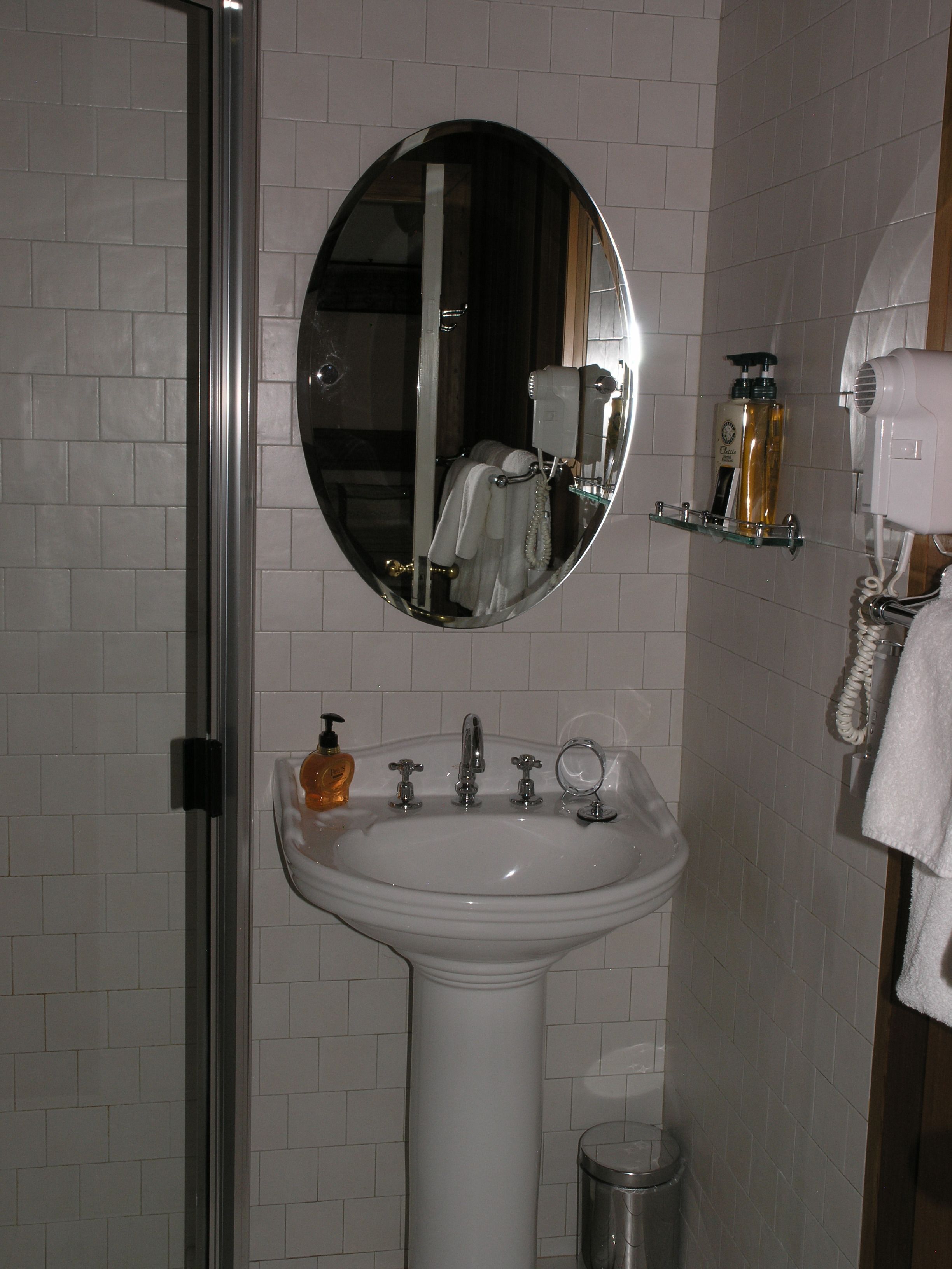 A bathroom with a white sink, a mirror, a hand dryer, and a soap dispenser.