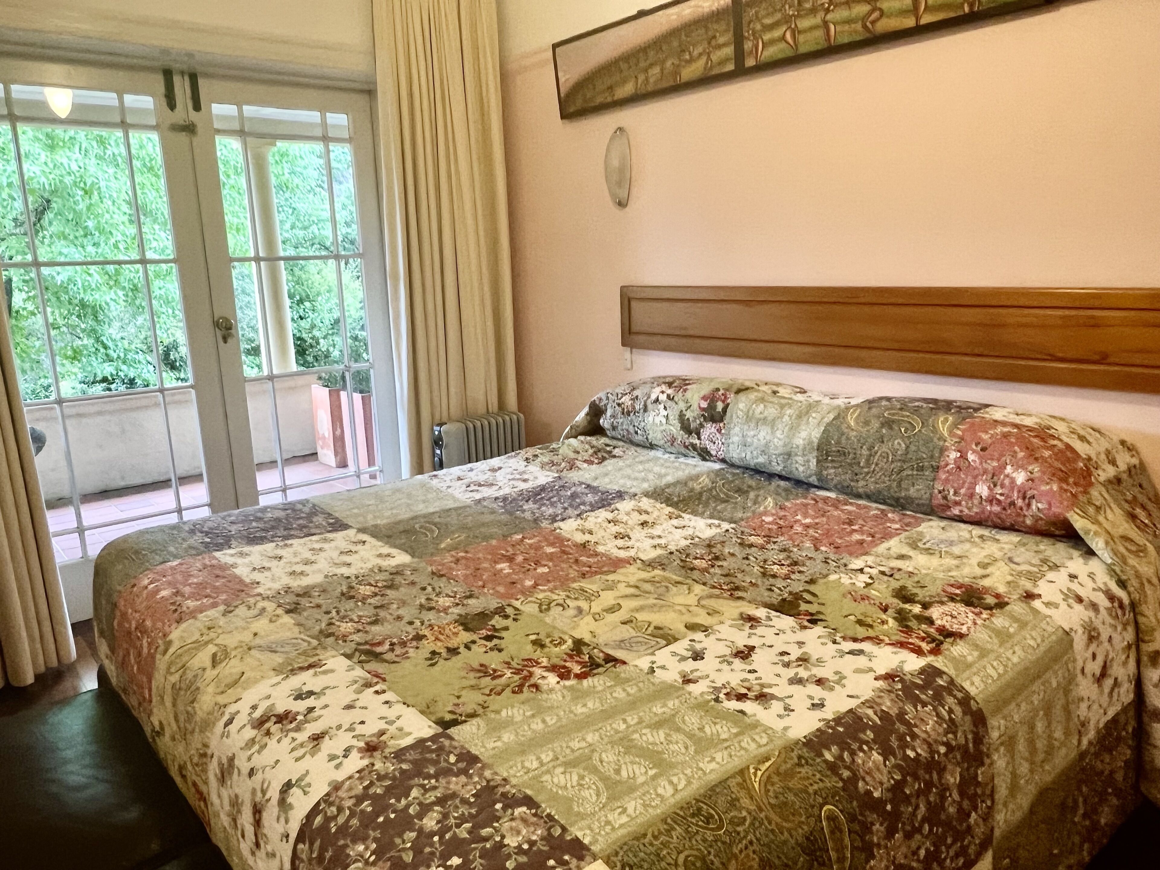 Een slaapkamer met een groot bed, een houten hoofdbord, een radiator en een raam met gordijnen.