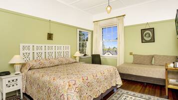 A bedroom with a large bed, a smaller sofa, a nightstand with a lamp, a chair, and a window with curtains.