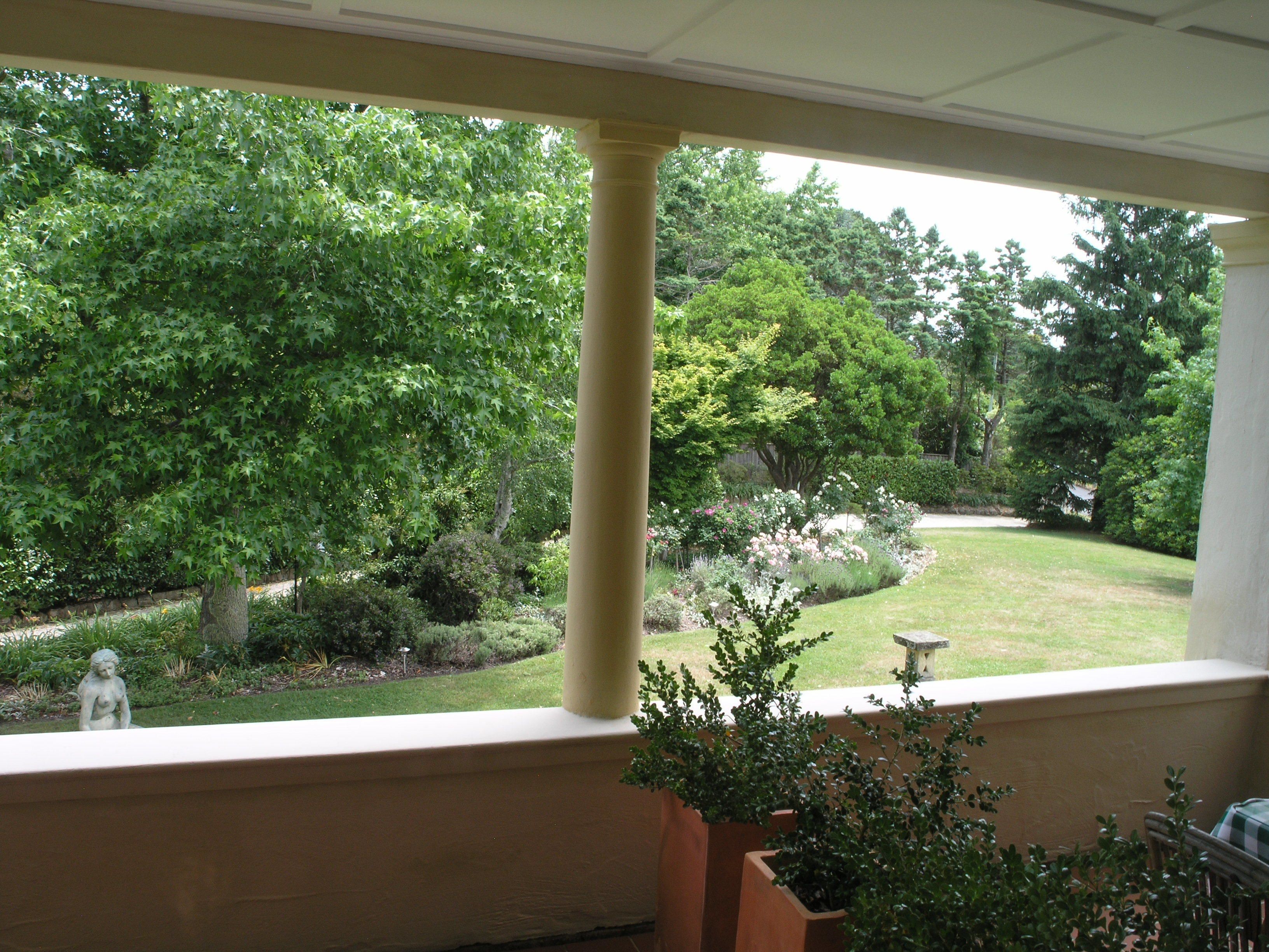 Vista desde una habitación con ventana que da a un jardín con diversas plantas y una estatua.