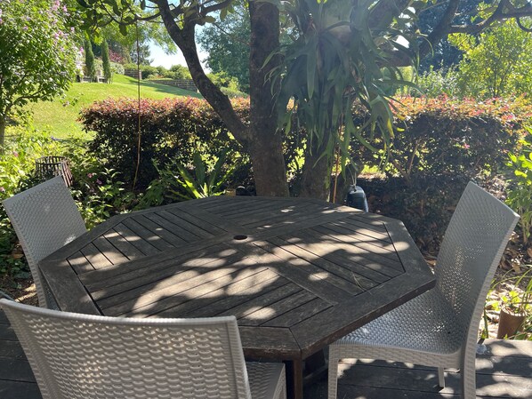 A wooden table with four chairs, surrounded by lush greenery and trees.