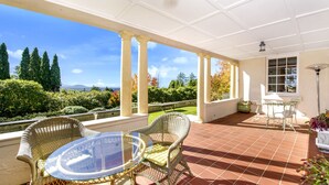 Un patio cubierto con muebles de mimbre, una mesa de vidrio y vistas al paisaje.