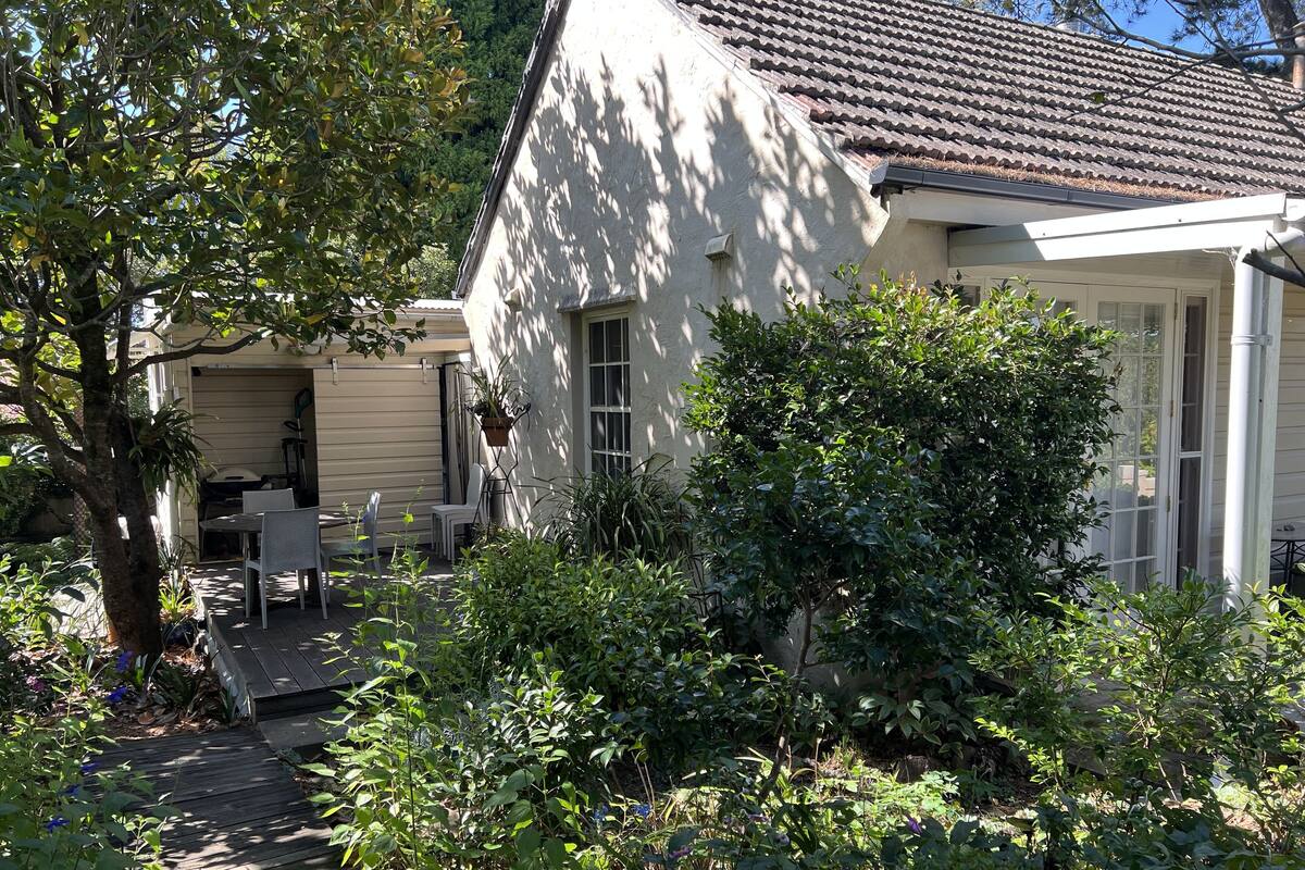 A house with a tiled roof, a covered patio with chairs, and a garden with various plants.