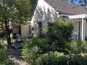 A house with a tiled roof, a covered patio with chairs, and a garden with various plants.