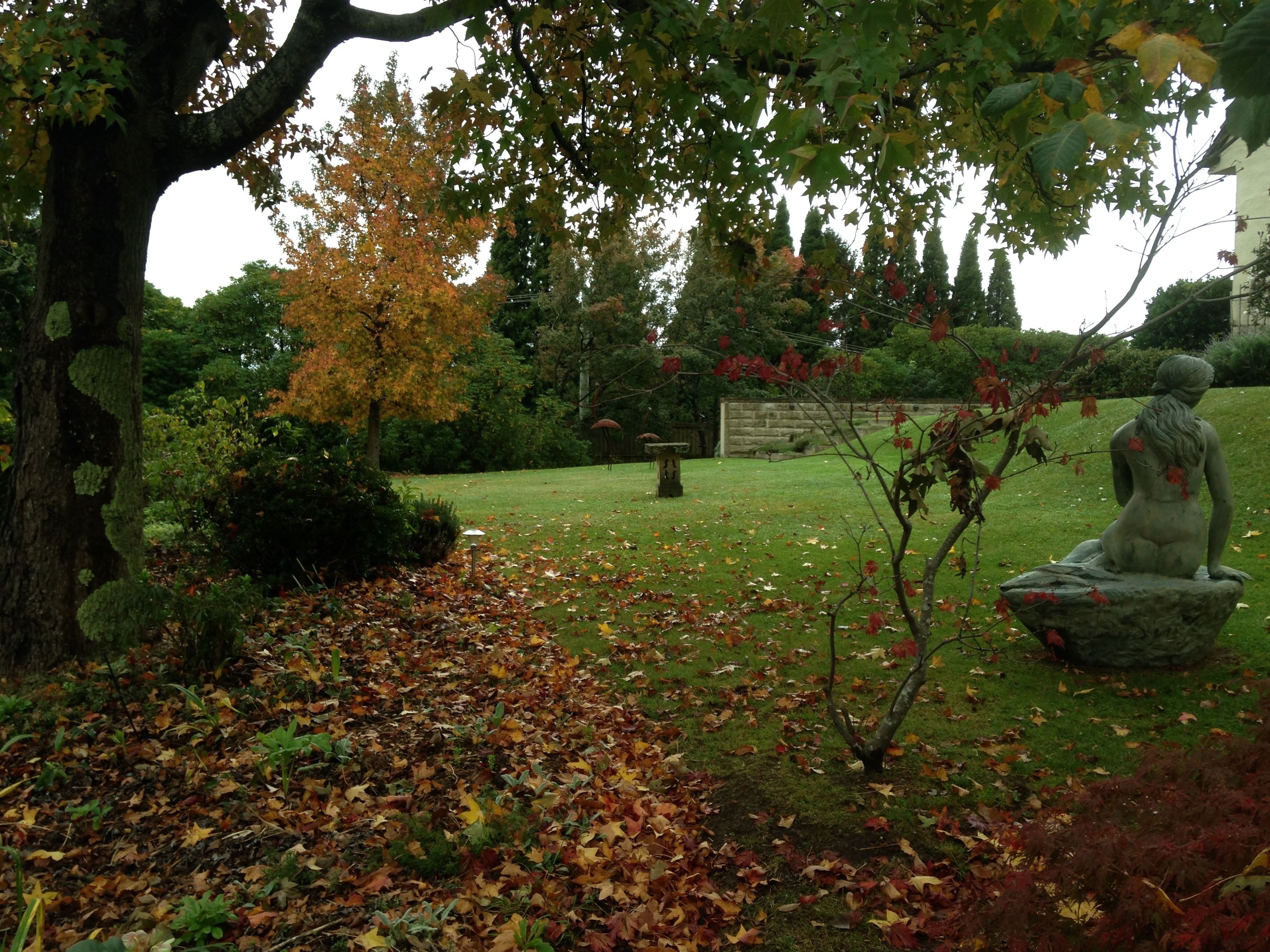 A statue of a seated figure in a garden with a tree and grass.