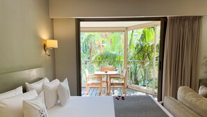A hotel room with a bed, a sofa, a balcony with a table and chairs, and a view of greenery. - Cannes Villa St Barth (Cannes)
