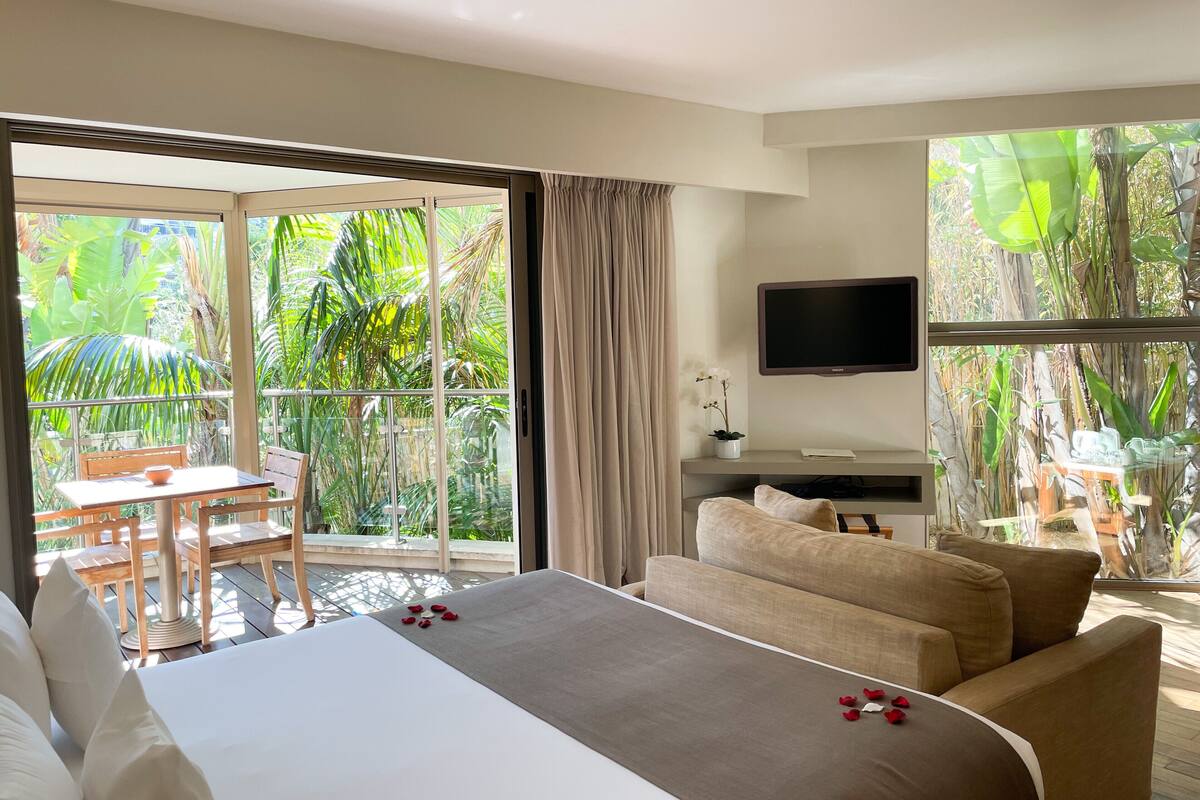A hotel room with a bed, a sofa, a TV, and a balcony with a table and chairs.