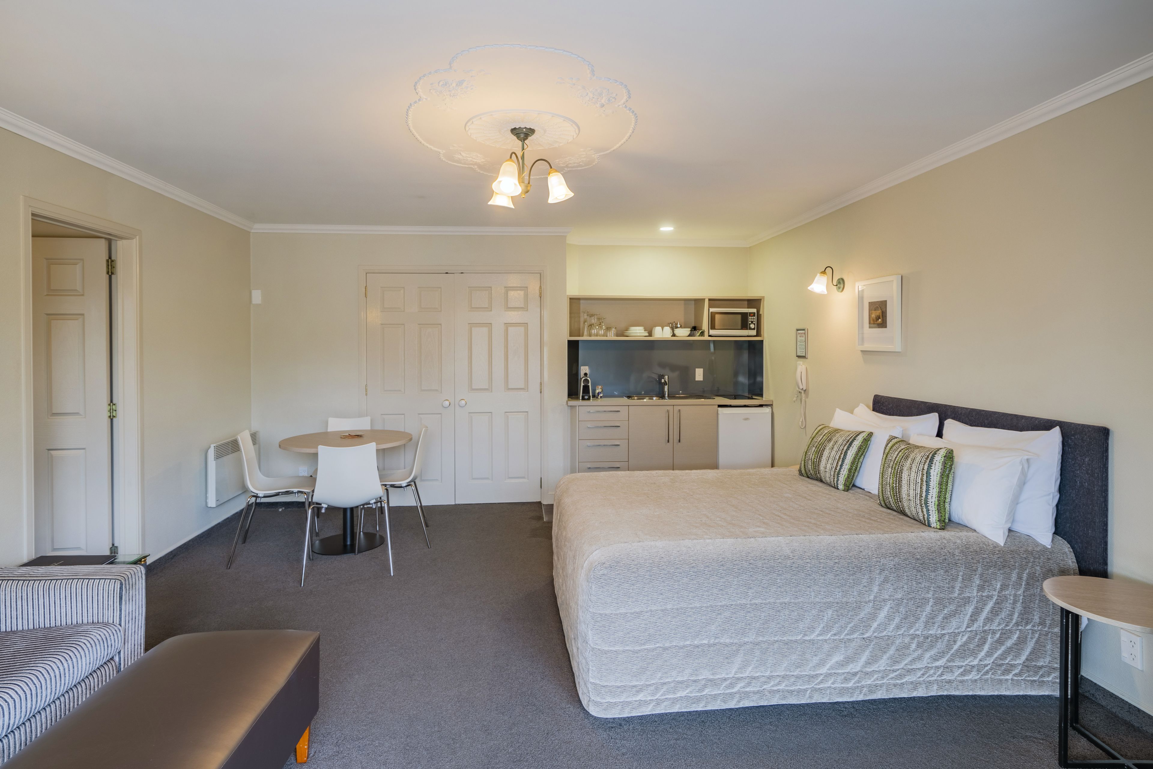 Habitación de hotel con cama, escritorio, silla, una mesita pequeña y kitchenette.