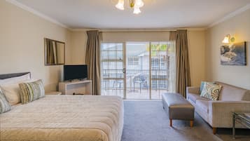 A hotel room with a large bed, a sofa, a TV, and a balcony with a view of the outside.