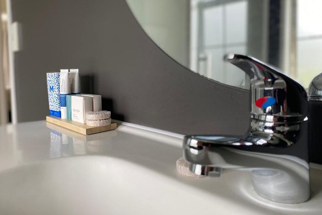 Un lavabo de salle de bain avec un robinet chromé, un miroir et un petit plateau en bois contenant des articles de toilette.