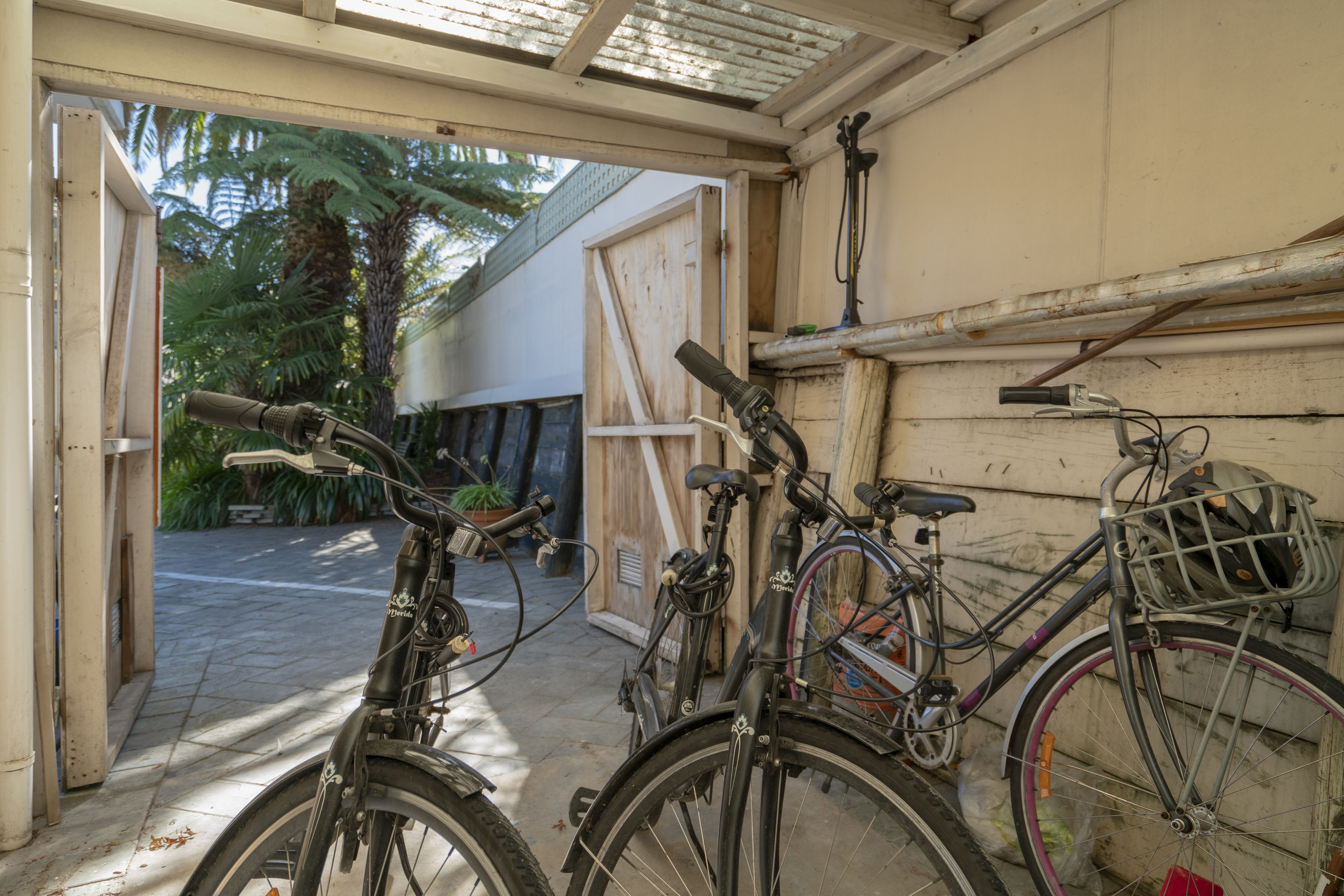 A bicycle parked in a garage with a wooden door and a metal roof.