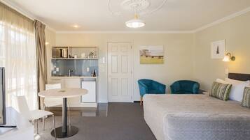 A hotel room with a bed, a desk, a chair, a small kitchenette, and a door.