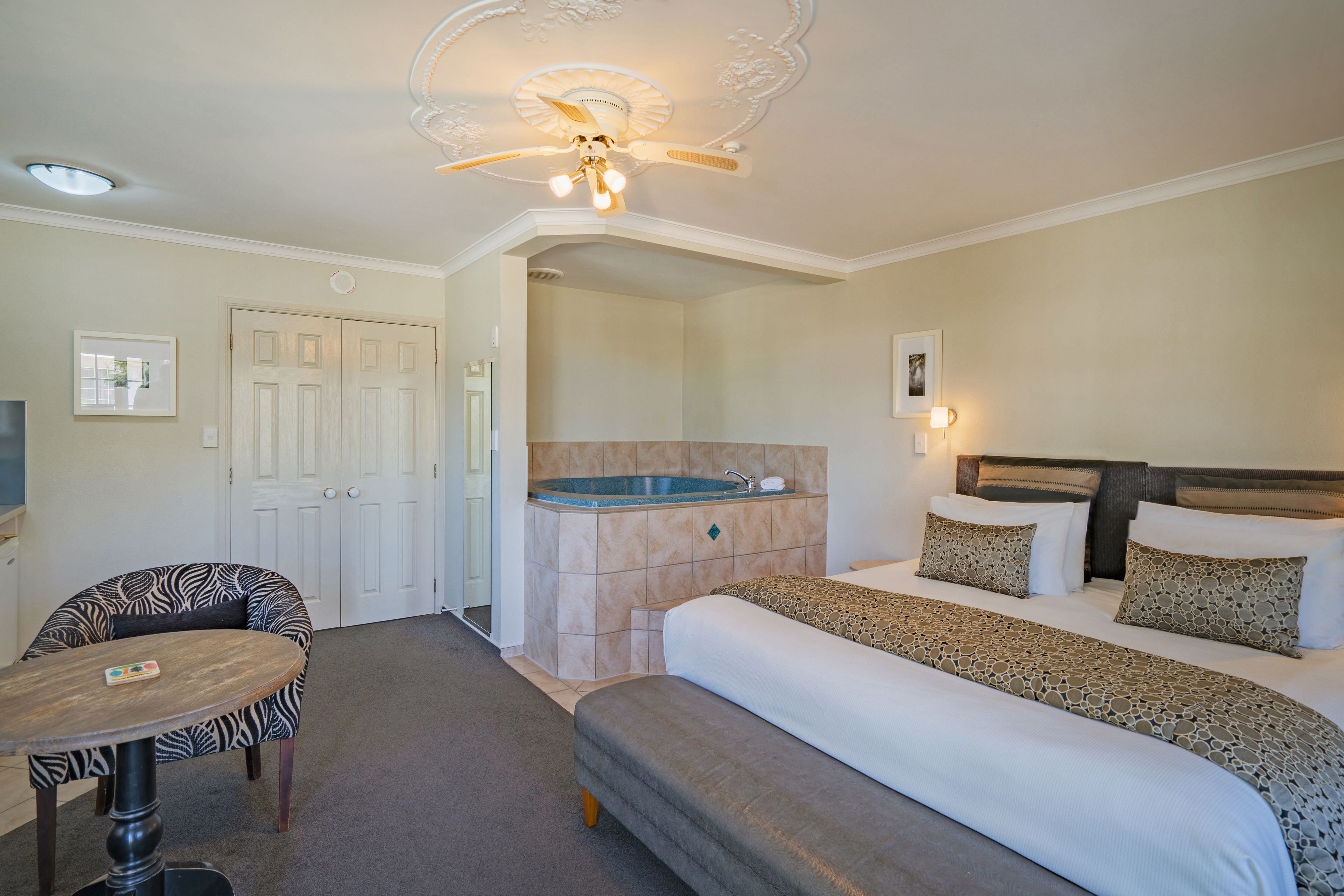Ein Hotelzimmer mit Bett, Sofa, kleinem Tisch, Deckenventilator, Badewanne und einer Tür.