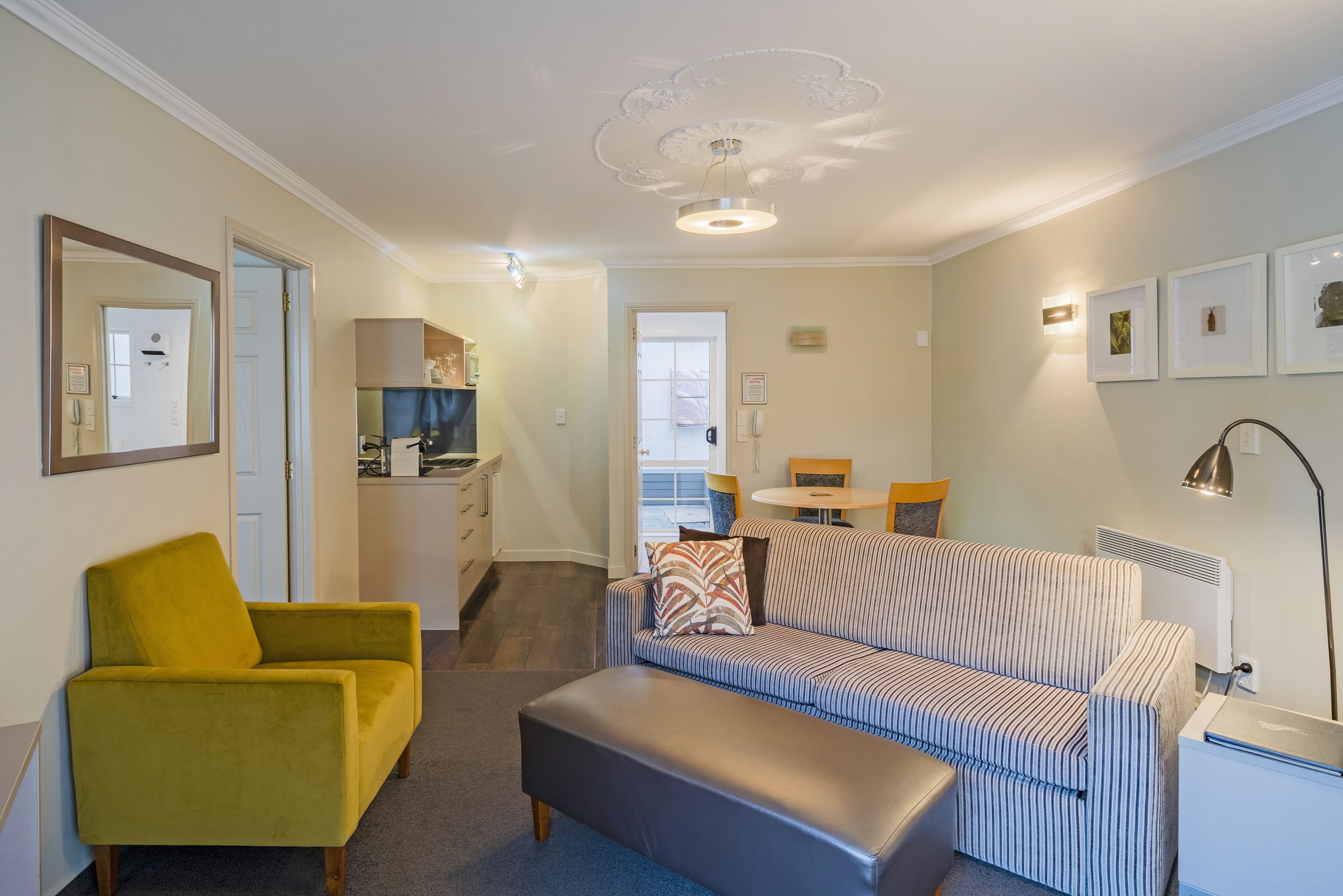 A compact living space with a sofa, a yellow armchair, a dining table, and a kitchenette.