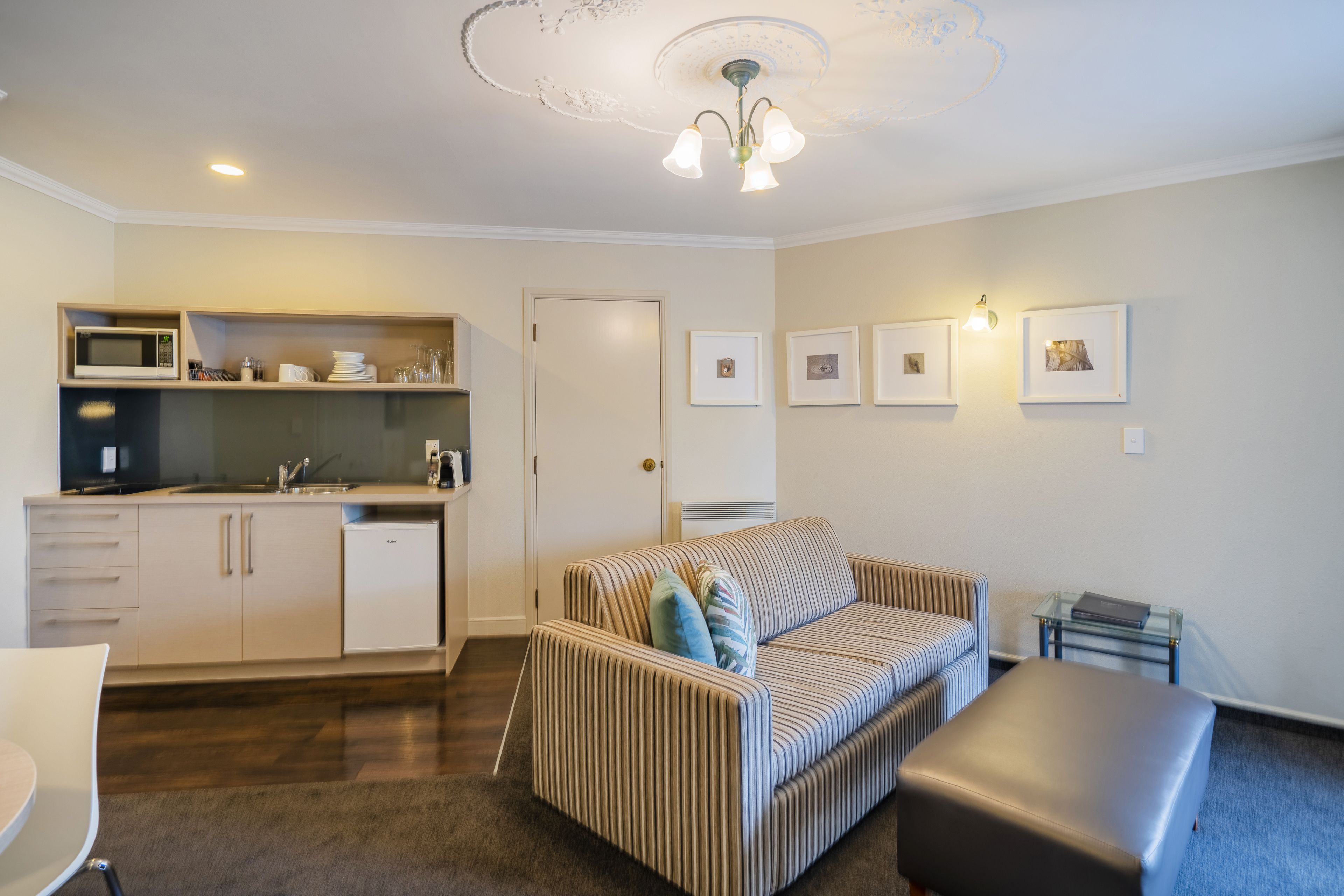 A compact living space with a kitchenette, a sofa, a glass coffee table, and a door.
