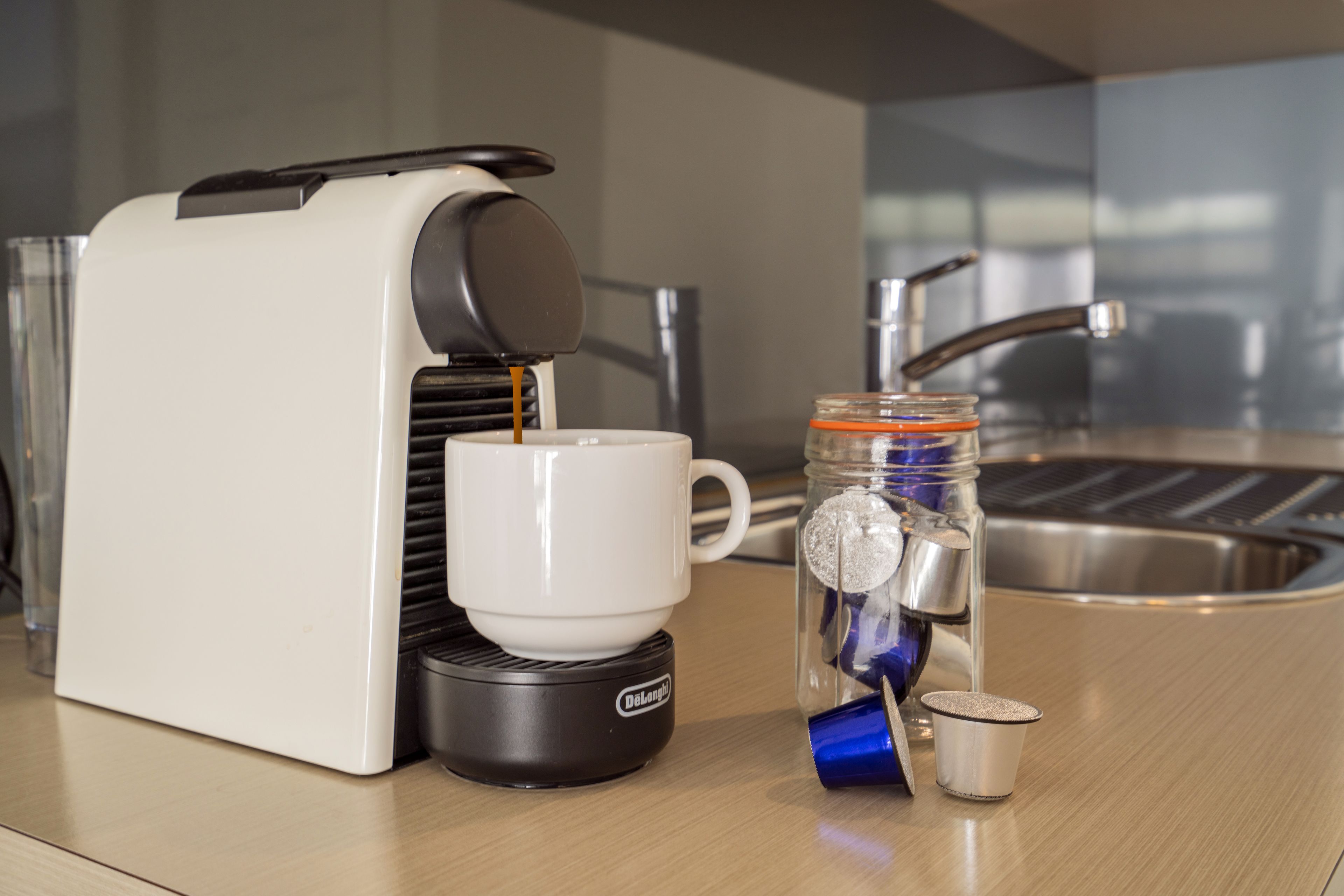 A coffee machine with a cup and a jar with a lid on a countertop.