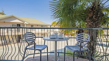A balcony with two chairs and a table, a palm tree, and a building in the background.