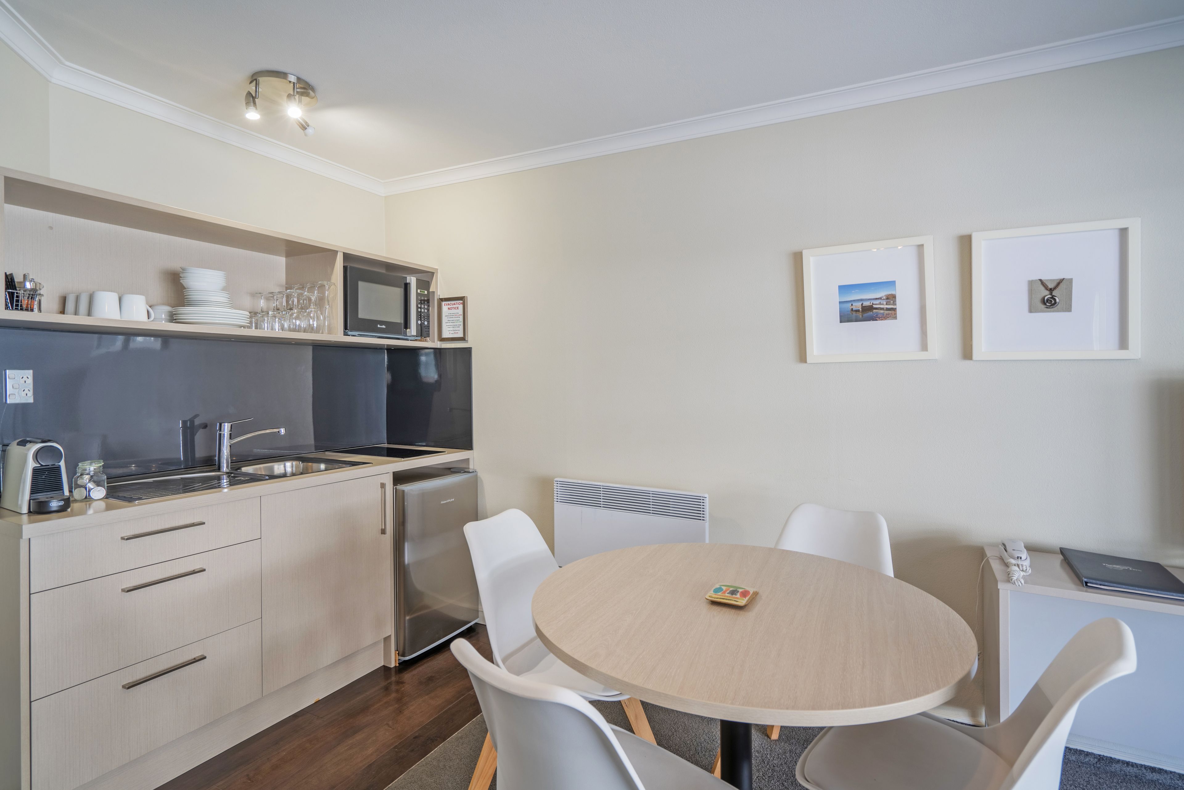 A modern kitchen with a microwave, sink, and stainless steel appliances. There is a dining table with chairs and a small clock on the table.