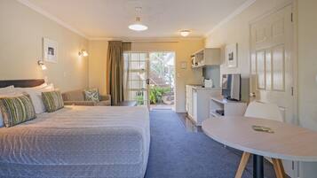 A hotel room with a large bed, a desk, a chair, and a small table. There is a door leading to a balcony.