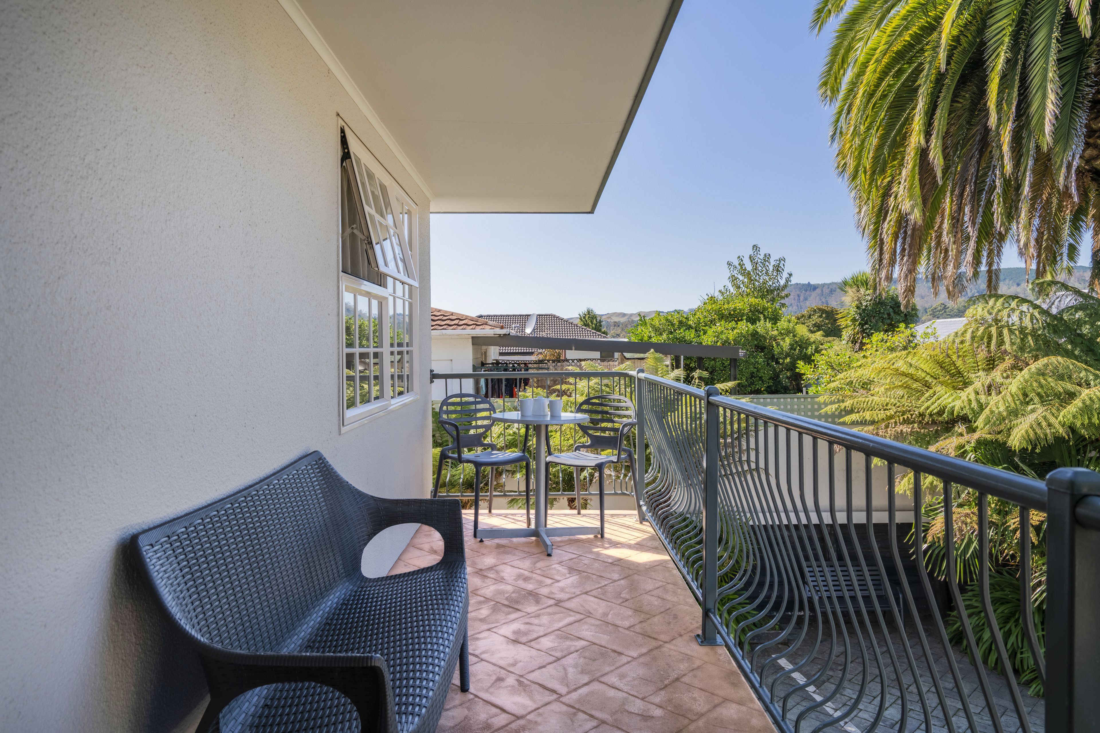 Un balcon avec une chaise, une table et une balustrade donnant sur un jardin planté de palmiers.