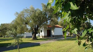 Un edificio pequeño con puerta roja, rodeado de árboles y césped.