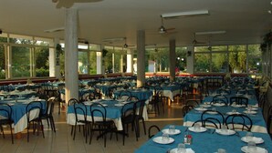 Un amplio comedor con varias mesas y sillas, ventanas grandes y ventiladores de techo.