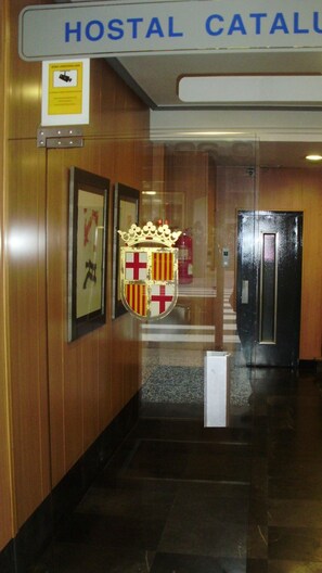 A hallway with a sign reading "HOSTAL CATALU" and a coat of arms on the wall.