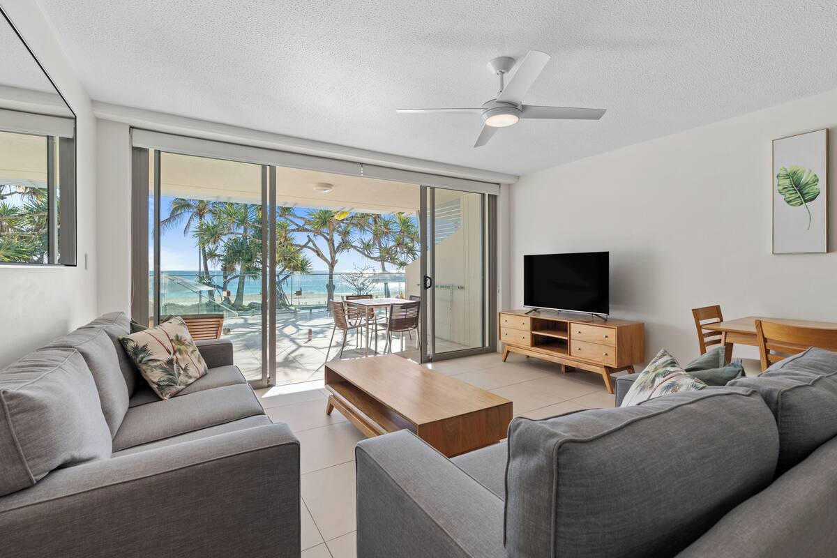A modern living room with a grey sofa, a wooden coffee table, and a flat-screen TV on a wooden stand.