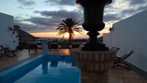 Una piscina en la azotea con sillas de descanso, un jarrón decorativo y vistas al atardecer.