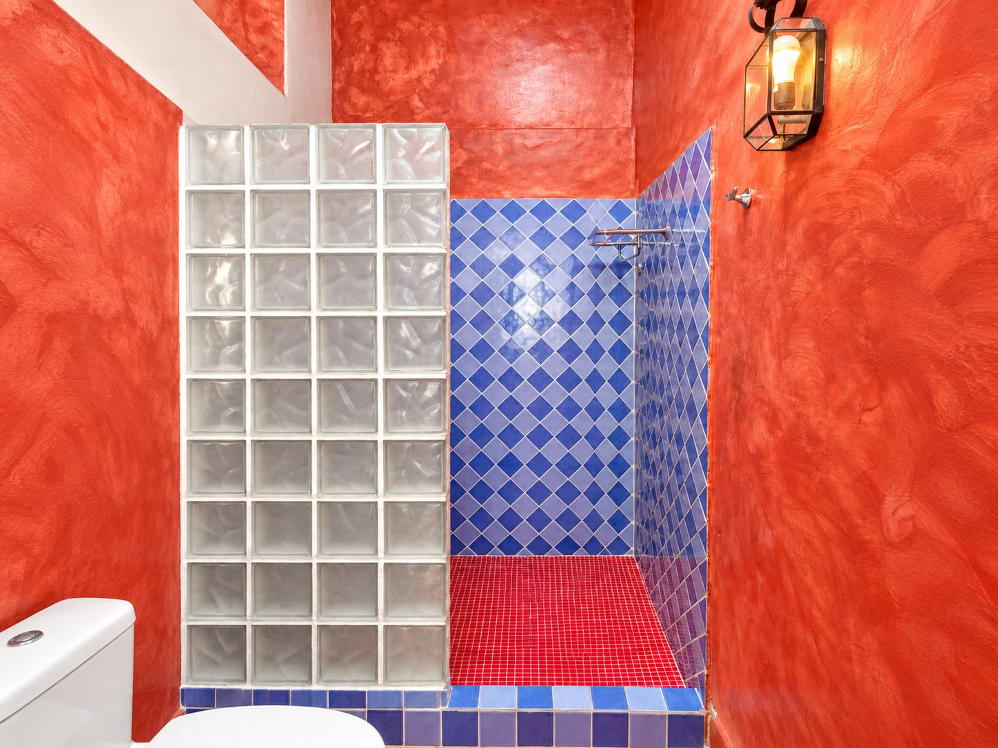 A bathroom with a glass shower enclosure, blue patterned tiles, and a red-tiled floor.