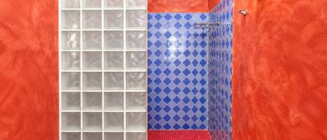 A bathroom with a glass shower enclosure, blue patterned tiles, and a red-tiled floor.